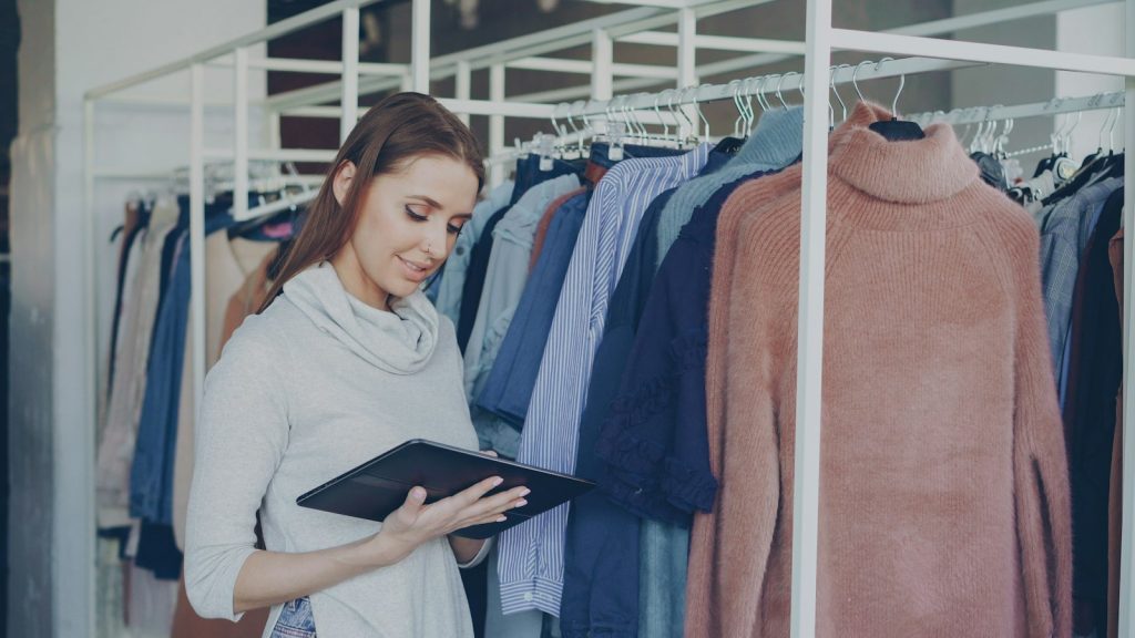 Une commerçante consulte sa tablette au milieu des portants de sa boutique